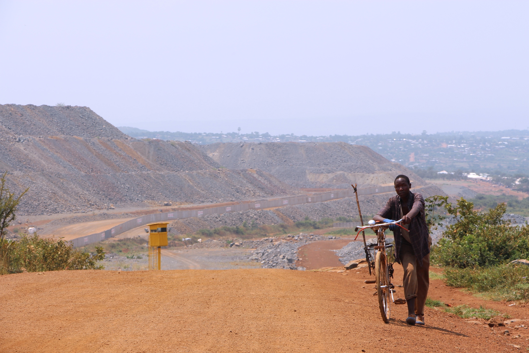 North Mara Gold Mine ligger like ved siden av småbyen Nyamongo i Mara-regionen nordvest i Tanzania. I bakgrunnen er muren som har blitt satt opp rundt det meste av gruven, samt et av vakttårnene som omringer den. Foto: Moses Matthews